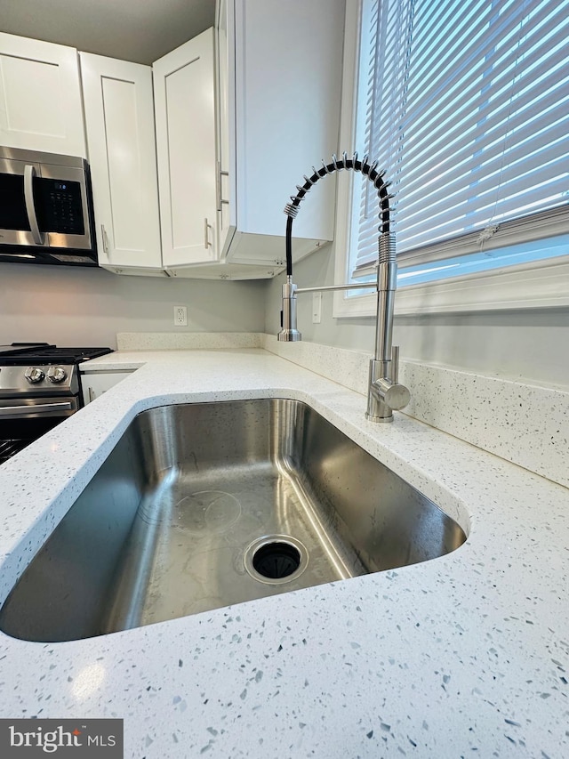 room details with white cabinets, stainless steel appliances, light stone counters, and sink