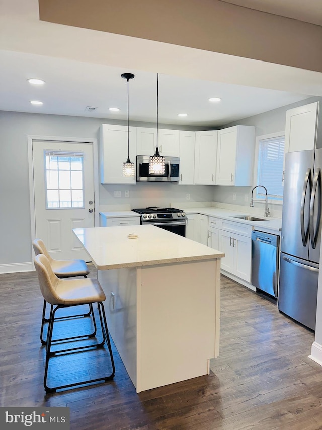 kitchen with a center island, dark wood-type flooring, hanging light fixtures, appliances with stainless steel finishes, and white cabinetry