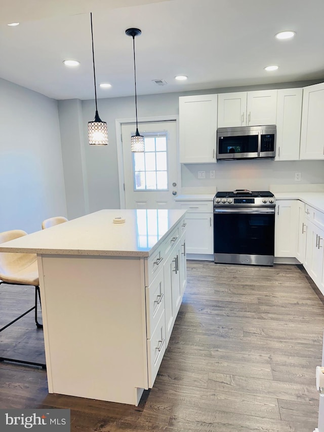 kitchen featuring appliances with stainless steel finishes, hardwood / wood-style flooring, white cabinets, hanging light fixtures, and a breakfast bar area