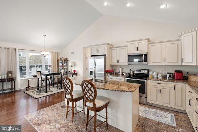 kitchen with dark hardwood / wood-style floors, stone counters, an island with sink, and appliances with stainless steel finishes