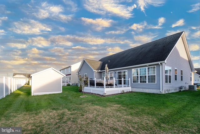 back house at dusk with a lawn and central AC unit