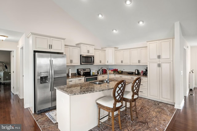 kitchen with appliances with stainless steel finishes, a center island with sink, dark hardwood / wood-style floors, and dark stone countertops