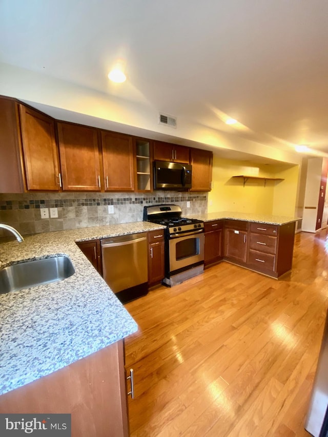 kitchen with appliances with stainless steel finishes, light hardwood / wood-style floors, light stone counters, and sink