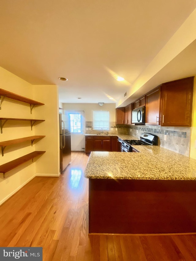 kitchen featuring kitchen peninsula, tasteful backsplash, light stone counters, stainless steel appliances, and light hardwood / wood-style floors