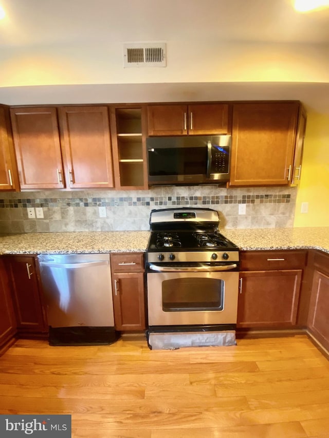 kitchen featuring decorative backsplash, light stone counters, light wood-type flooring, and appliances with stainless steel finishes