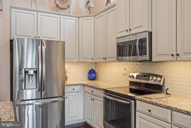 kitchen featuring stainless steel appliances, white cabinetry, tasteful backsplash, and light stone counters