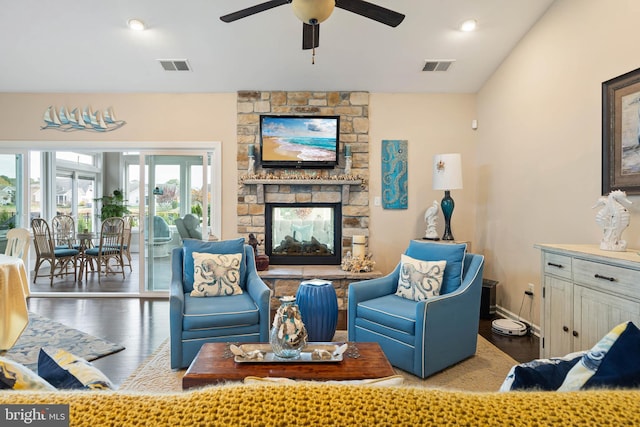 living room featuring wood-type flooring, a stone fireplace, ceiling fan, and a healthy amount of sunlight