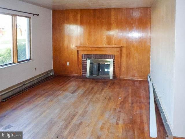115 Mountain View Rd, Armagh, PA 15920 - unfurnished living room featuring a brick fireplace, wood finished floors, wooden walls, and a baseboard radiator