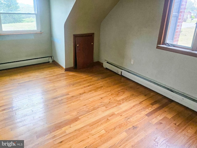 additional living space featuring baseboard heating, vaulted ceiling, and light wood-type flooring