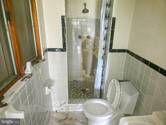 bathroom with toilet, tiled shower, and tile walls