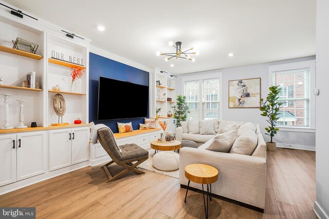 living room with a notable chandelier, ornamental molding, built in shelves, and light hardwood / wood-style flooring