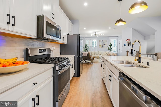 kitchen featuring white cabinetry, sink, light hardwood / wood-style flooring, decorative light fixtures, and appliances with stainless steel finishes