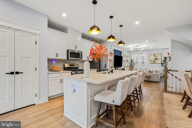 kitchen featuring an island with sink, stainless steel appliances, decorative light fixtures, and light hardwood / wood-style floors