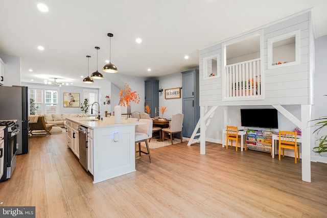 kitchen featuring a kitchen bar, a center island with sink, white cabinets, and light wood-type flooring