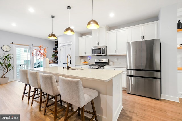 kitchen with a kitchen island with sink, white cabinets, sink, appliances with stainless steel finishes, and light hardwood / wood-style floors