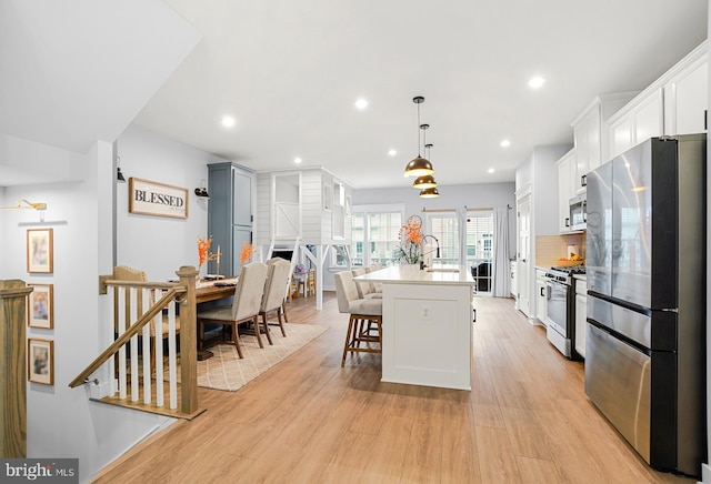 kitchen with appliances with stainless steel finishes, a breakfast bar, pendant lighting, a center island with sink, and light hardwood / wood-style flooring