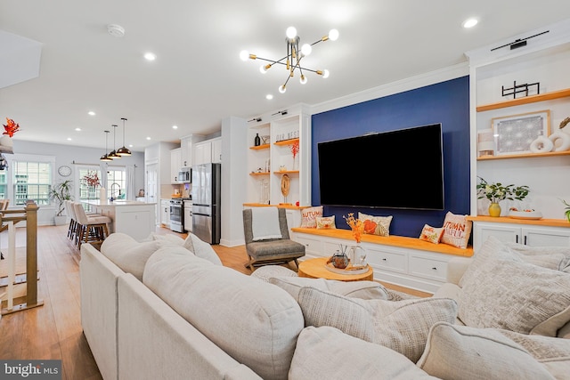 living room with light hardwood / wood-style floors, an inviting chandelier, ornamental molding, and sink