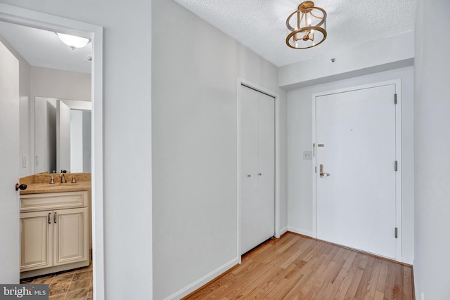 foyer featuring a chandelier, sink, light hardwood / wood-style floors, and a textured ceiling