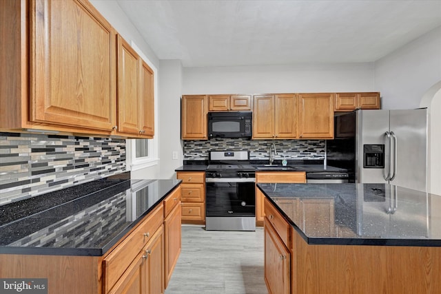 kitchen featuring sink, stainless steel appliances, dark stone countertops, decorative backsplash, and light wood-type flooring