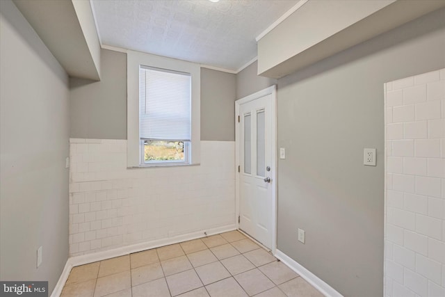 empty room featuring a textured ceiling, light tile patterned floors, tile walls, and ornamental molding