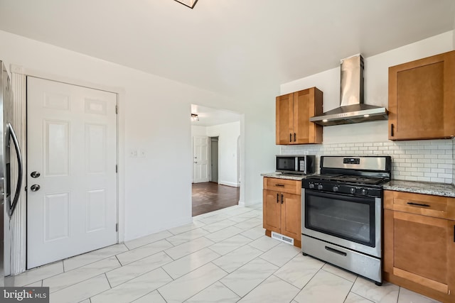 kitchen with stainless steel range with gas cooktop, light stone counters, wall chimney range hood, and backsplash