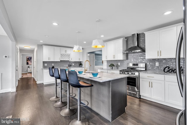 kitchen with stainless steel gas stove, wall chimney exhaust hood, white cabinets, and hanging light fixtures