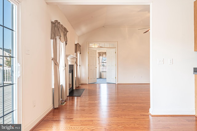 foyer entrance featuring light wood-style floors, a fireplace with flush hearth, vaulted ceiling, and a wealth of natural light