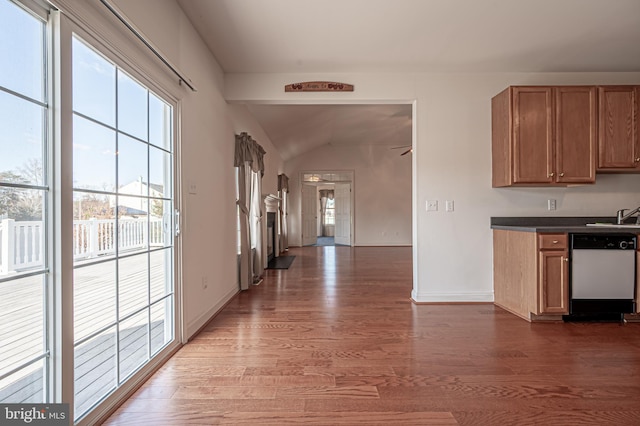 kitchen with dark countertops, brown cabinetry, white dishwasher, wood finished floors, and baseboards