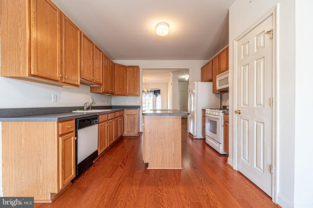 kitchen featuring white appliances, a sink, a center island, dark wood-style floors, and dark countertops