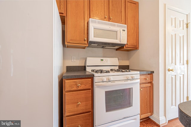 kitchen with dark countertops, white appliances, and brown cabinets