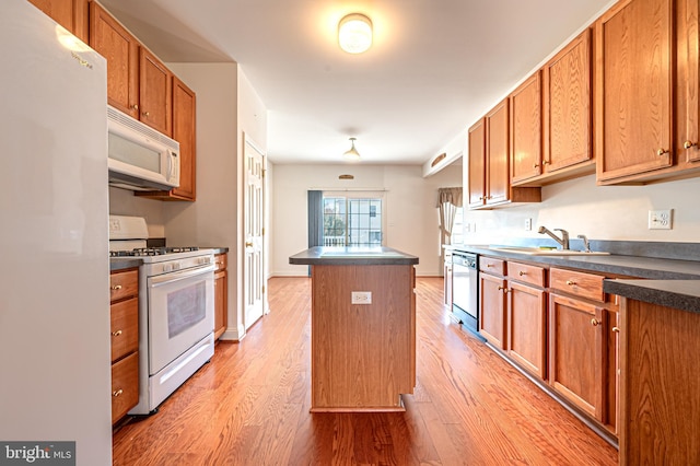 kitchen with white appliances, a sink, light wood-style floors, a center island, and dark countertops