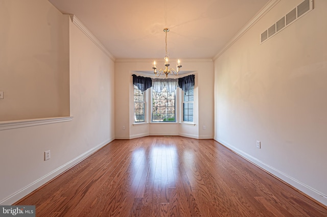 empty room featuring baseboards, visible vents, a notable chandelier, and wood finished floors