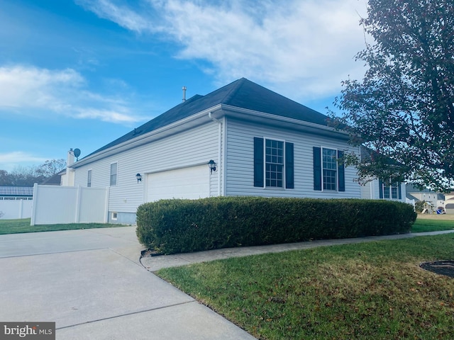 view of side of property featuring concrete driveway, fence, an attached garage, and a lawn