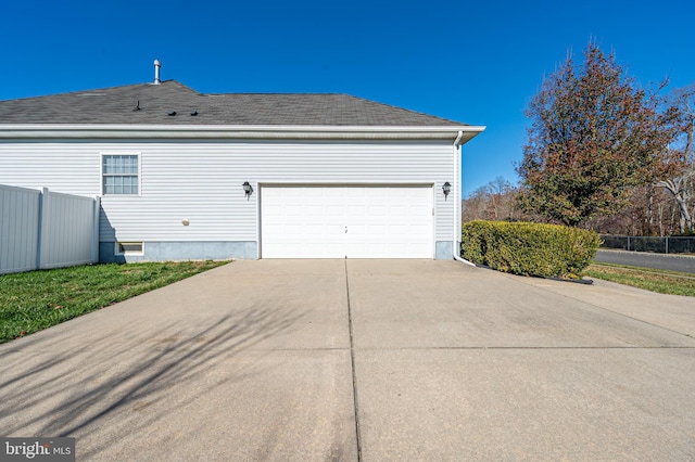 view of side of property with a garage, a shingled roof, fence, and concrete driveway