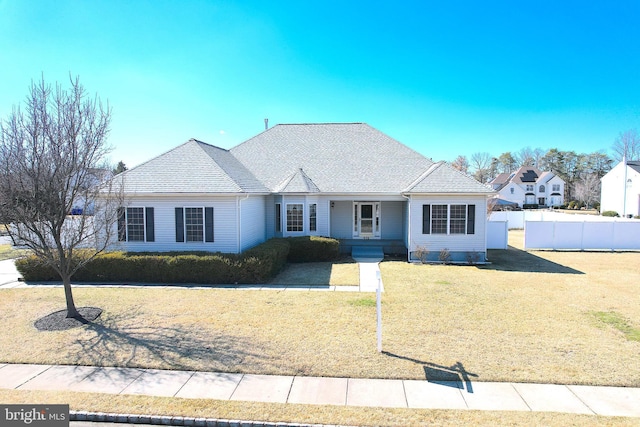 ranch-style home with a front lawn, roof with shingles, and fence