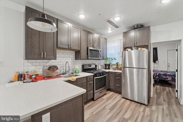 kitchen with sink, hanging light fixtures, light hardwood / wood-style flooring, appliances with stainless steel finishes, and kitchen peninsula