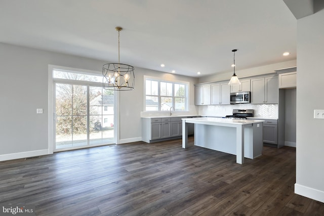 kitchen with gray cabinetry, dark wood-type flooring, appliances with stainless steel finishes, decorative light fixtures, and a kitchen island