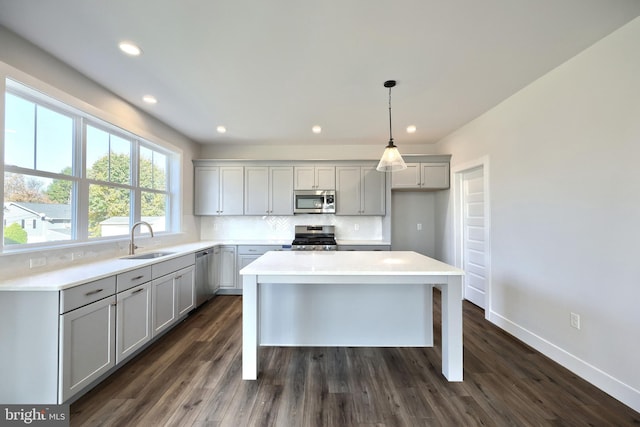 kitchen with sink, gray cabinets, appliances with stainless steel finishes, a kitchen island, and dark hardwood / wood-style flooring