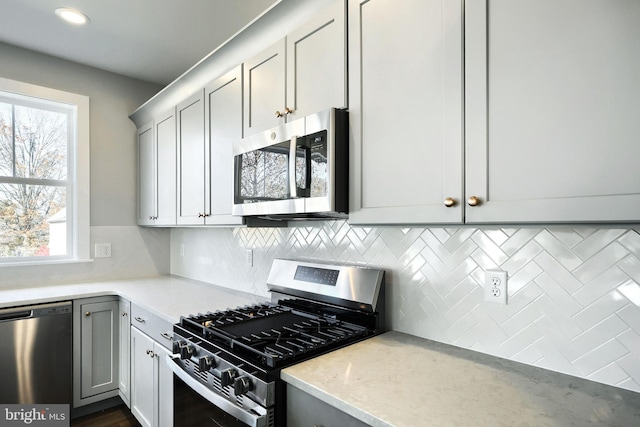 kitchen featuring backsplash, gray cabinets, light stone countertops, and stainless steel appliances