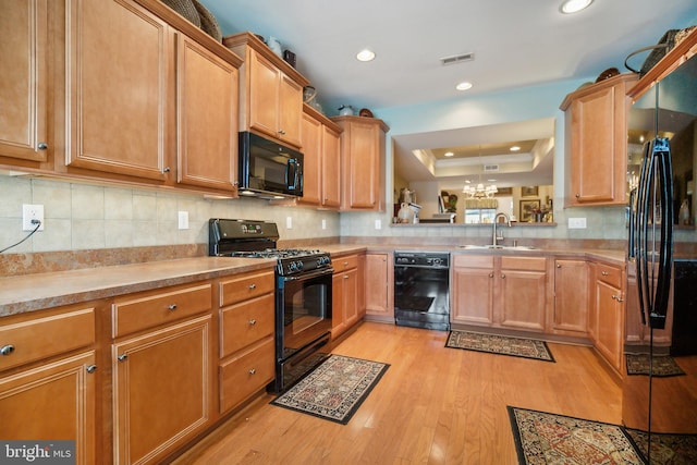 kitchen with tasteful backsplash, a raised ceiling, sink, black appliances, and light hardwood / wood-style flooring