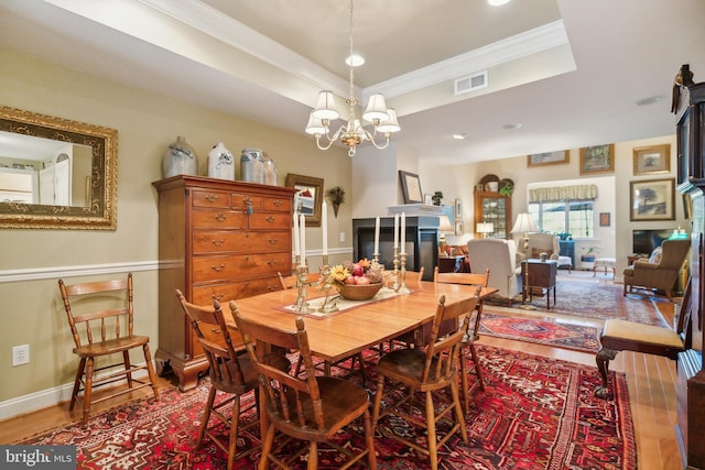 dining room with wood-type flooring, a tray ceiling, ornamental molding, and a notable chandelier