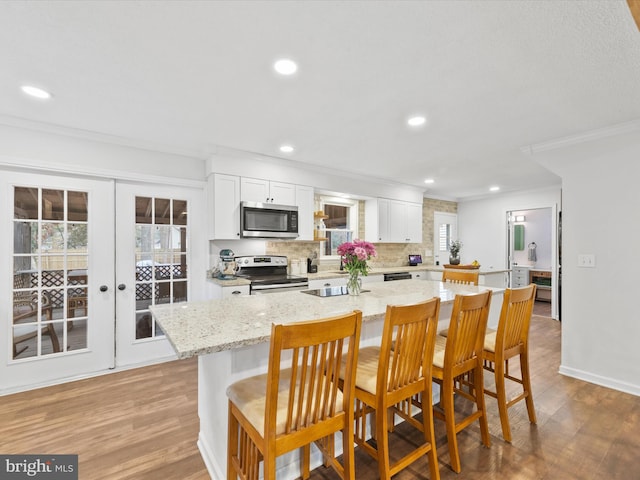 kitchen featuring light stone counters, french doors, a breakfast bar area, appliances with stainless steel finishes, and white cabinetry