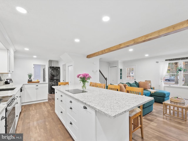 kitchen featuring a breakfast bar, a sink, white cabinetry, open floor plan, and stacked washer and clothes dryer