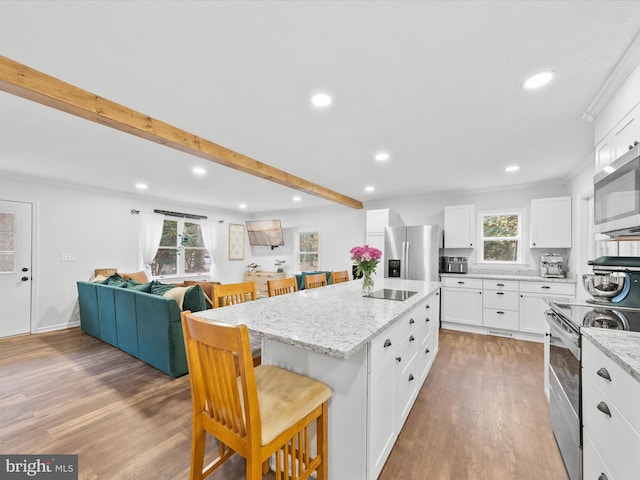 kitchen with appliances with stainless steel finishes, open floor plan, a kitchen breakfast bar, a center island, and light stone countertops