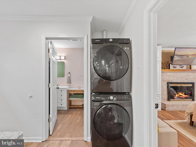 clothes washing area featuring light wood-style flooring, laundry area, ornamental molding, a brick fireplace, and stacked washer and clothes dryer