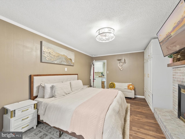 bedroom featuring a textured ceiling, ornamental molding, a brick fireplace, and wood finished floors