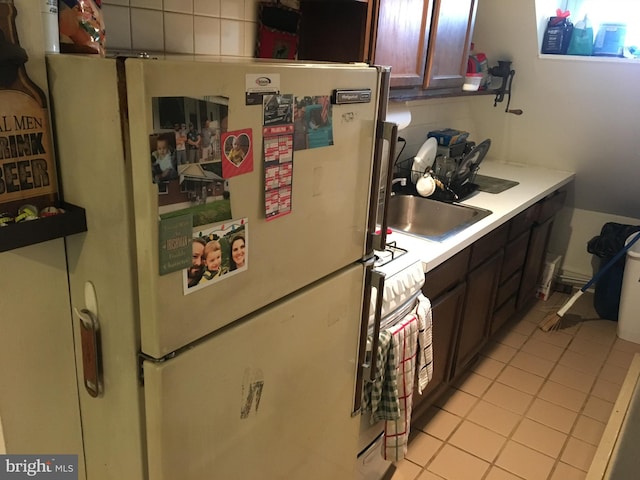 kitchen featuring dark brown cabinets, stove, light tile patterned floors, and fridge