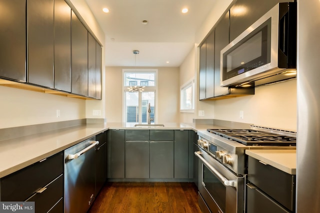 kitchen featuring sink, dark hardwood / wood-style floors, appliances with stainless steel finishes, decorative light fixtures, and kitchen peninsula