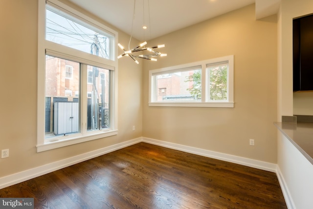 empty room featuring dark hardwood / wood-style floors, a healthy amount of sunlight, and a notable chandelier