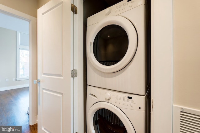 clothes washing area featuring stacked washer / dryer and dark wood-type flooring